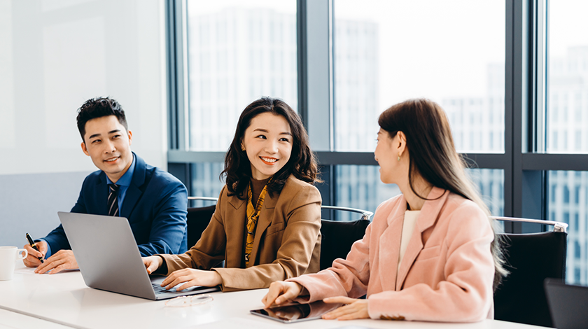 Three employees in an office environment. Two women are discussing something on screen.