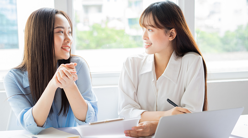 Two women have a discussion while standing in an office
