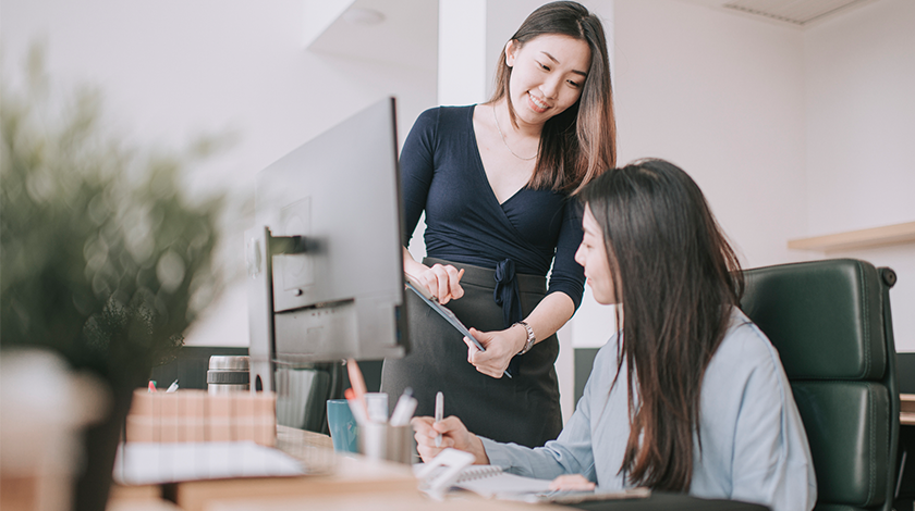 Two women have a discussion while standing in an office